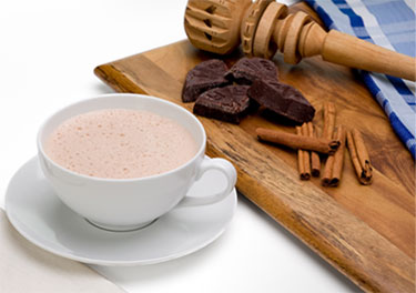 Taza de chocolate e ingredientes: chocolate en barra, canela y molinillo